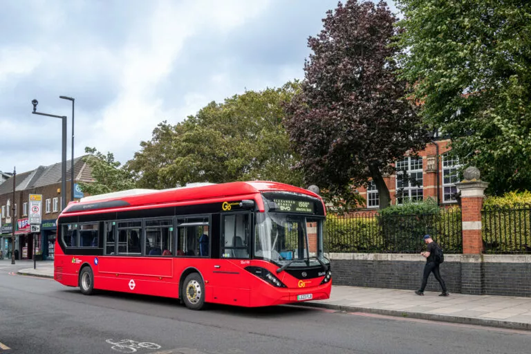 A red single deck bus which has 'Alexander Dennis BYD 1500th electric bus' on its display stands on a suburban street
